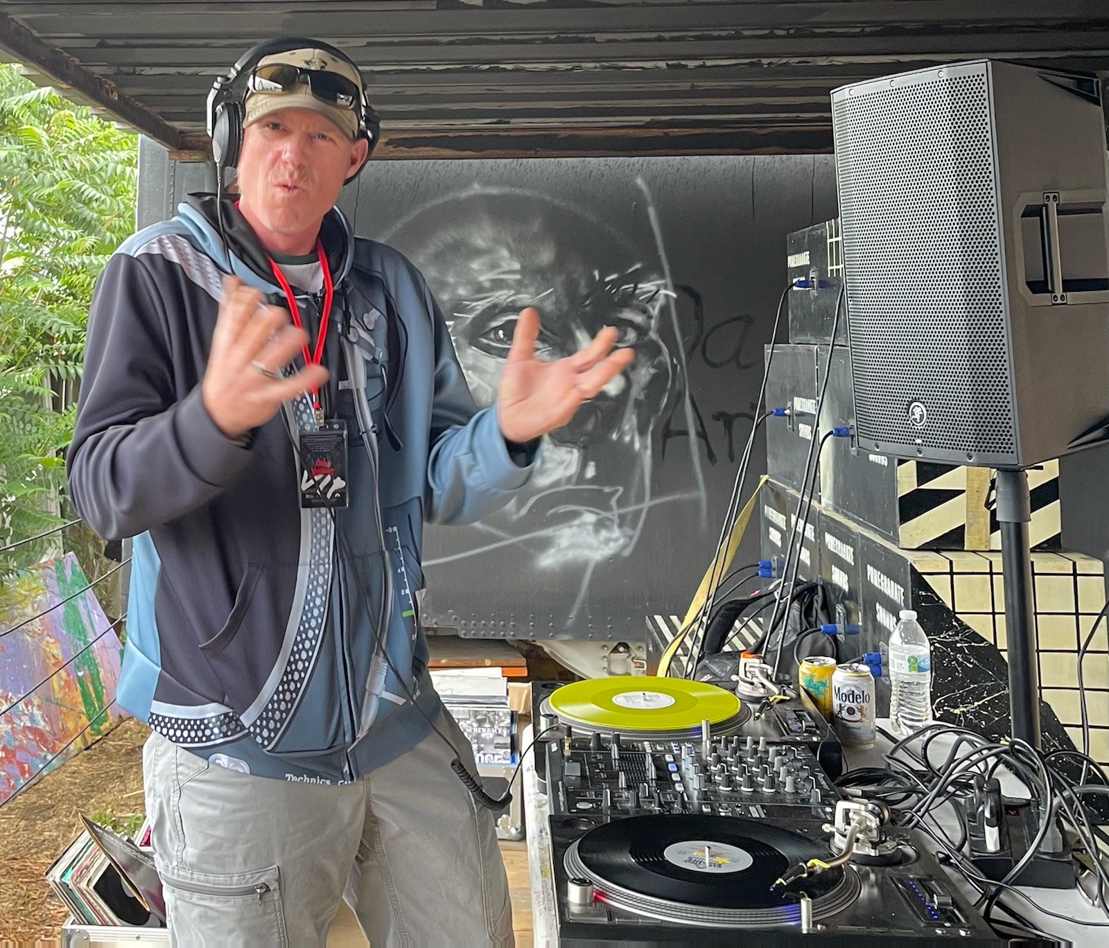 DJ Natural Nate® at an outdoor set with yellow vinyl, graffiti mural backdrop, and Technics setup